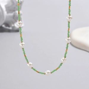 Macro shot of bohemian necklace featuring white pearls, green beads, and gold accents