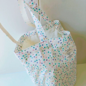 Detail einer cremefarbenen Baumwolltasche mit bunten Punkten und Textiletikett