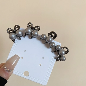 Close-up of mini gunmetal pearl hair clips with bow designs on a display card
