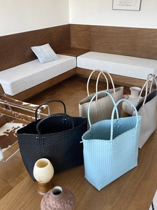 Close-up of handmade straw woven tote bags in black, light blue, beige, and grey colors