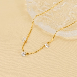 Detail of gold chain necklace featuring three round cubic zirconia stones on textured fabric