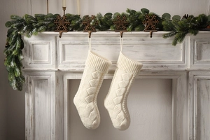 Detail of two white cable knit Christmas stockings hanging on a rustic fireplace