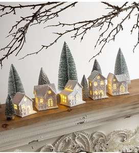 Luminous miniature Christmas snow houses and pine trees on a rustic mantel display