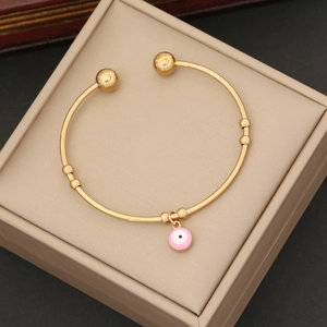 Detail view of a gold open bangle featuring a pink enamel evil eye charm in a jewelry box