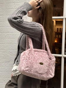 Sac à épaule chic en fausse fourrure léopard rose porté par un mannequin contre un mur blanc