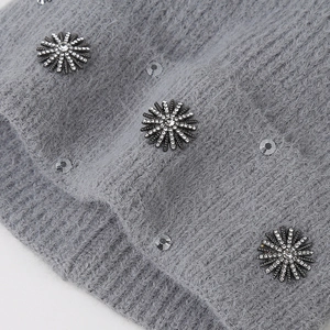 Close-up of grey knit hat fabric with plush texture and floral rhinestone embellishments