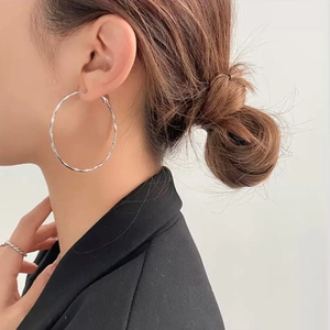 Close-up of large silver hoop earrings with twisted texture worn by a model in a black suit