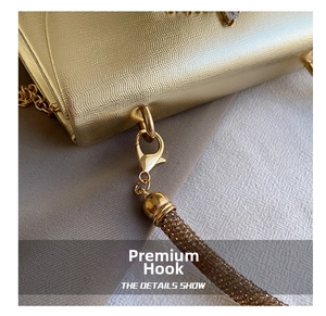 Detail of lizard-embossed gold clutch with rhinestone-studded strap and premium metal hook