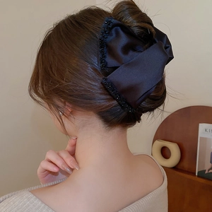 Detail of a large black silk bow hair claw clip with delicate bead trim on a model