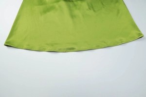 Detailed view of the green satin dress hem showing smooth silk texture and fine stitching
