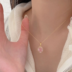 Close-up of a pink oval gemstone necklace with a gold chain worn on a sweater