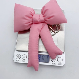 Close-up of a pink stuffed bow keychain weighing 20.1g on a digital scale for bags