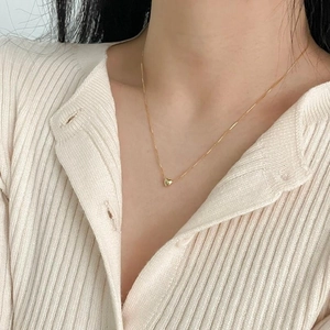 Close-up of a minimalist gold heart pendant necklace worn on a cozy knit cardigan