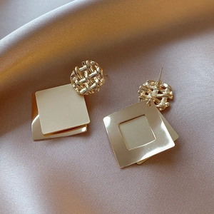 Detail of gold geometric earrings with woven studs and square sequins on silk background