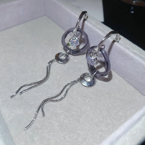 Détail de boucles d'oreilles C argentées avec anneau acrylique violet, zircon et longs glands
