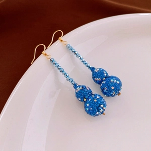 Detail view of blue rhinestone gourd tassel earrings with gold-tone hooks on white porcelain