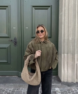 Detail of an olive green faux suede jacket and a beige woven handbag for women