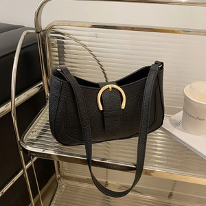 Detail of black lychee texture underarm bag with gold D-buckle on a glass shelf