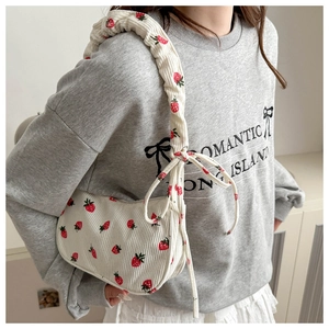 Detail of white corduroy shoulder bag with strawberry print and zipper closure on model