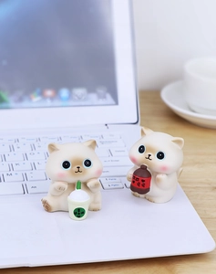 Close-up of cute cream cat figurines holding milk tea on a white laptop keyboard