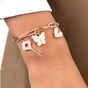 Close-up of gold charm bracelet with pink butterfly, heart and key pendants on wrist