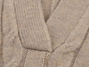 Macro detail of beige chunky cable knit texture and ribbed V-neckline on a soft polo sweater