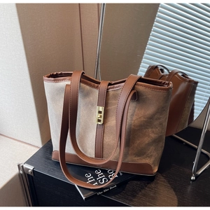 Detail of canvas tote bag with brown leather trim and golden metal twist lock closure
