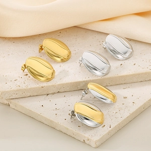 Close-up of gold, silver, and bicolor oval stud earrings on beige silk and stone