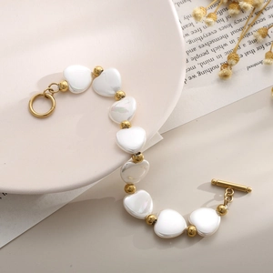 Détail du fermoir OT doré et des perles de cœur blanches sur un bracelet en titane