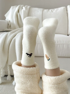 Detail of white plush socks featuring cute puppy and carrot embroidery on warm fabric