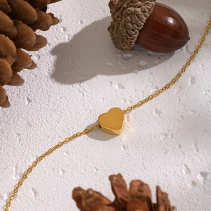 Close-up of golden heart pendant necklace on white surface with pinecone decor
