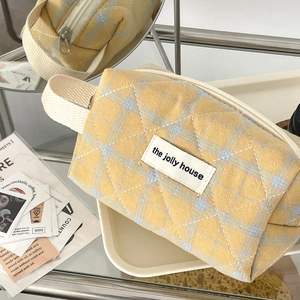 Detail of yellow quilted plaid makeup bag with woven handle and metal zipper closure