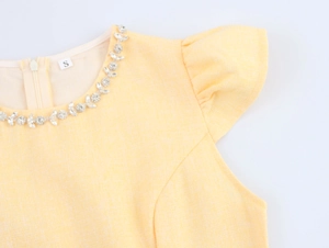 Dettaglio vestito giallo con scollo rotondo decorato con strass e maniche con volant raffinate
