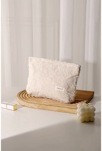 Detail of cream corduroy makeup bag with lace embroidery on a wooden tray with lipstick