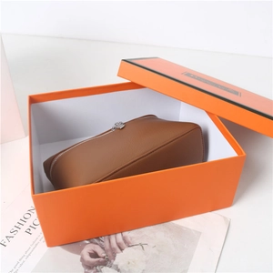 Detailed view of a brown pebbled leather cosmetic bag inside a luxury orange gift box