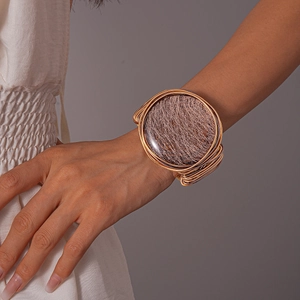 Macro detail of gold braided geometric wide cuff bracelet with textured metallic center disk