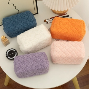 Detailed flat lay of quilted plush makeup bags in five soft pastel colors on a vanity desk