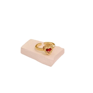 Adjustable golden ring with red heart gemstone and crown thorny detail on marble base