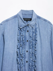 Macro detail of denim shirt featuring ruffled front trim and classic black buttons