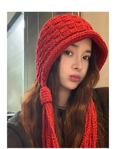 Close-up of red chunky knit earflap hat with long handmade braided tassels