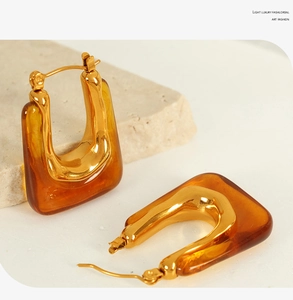 Detailed close-up of U-shaped gold earrings with amber resin on stone background