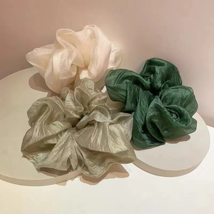 Three elegant silk organza scrunchies in cream and green shades on a stone tray