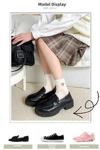 Detail of black platform loafers and white embroidered socks on beige carpet