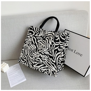 Detail shot of zebra print canvas tote bag featuring black fabric handles on a grey surface