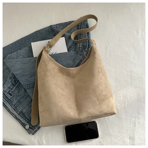 Flat lay of beige suede tote bag with denim jacket and smartphone on white fabric