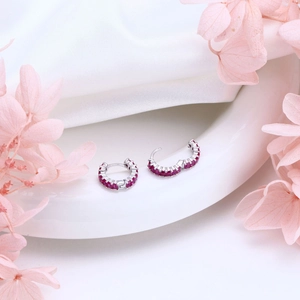 Detail of silver hoop earrings with red zircon stones on a white ceramic display