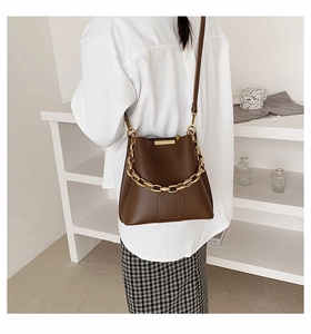 Detailed view of deep brown leather bucket bag with chunky gold chain strap accent