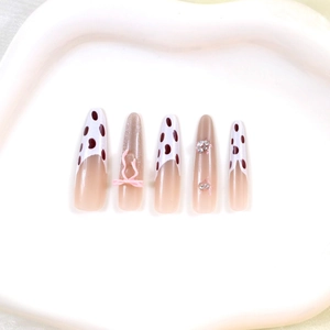 Détail de faux ongles ballerine longs avec nœuds roses, motif vache et strass brillants