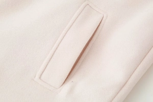 Detailed close-up of pocket stitching on a light pink wool coat with soft texture