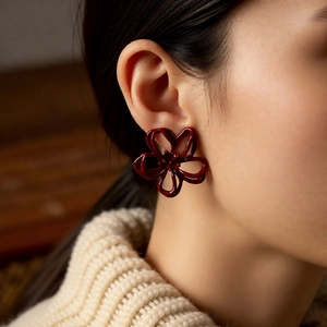Close-up of deep red hollow flower earring worn by a model in a cozy, elegant setting